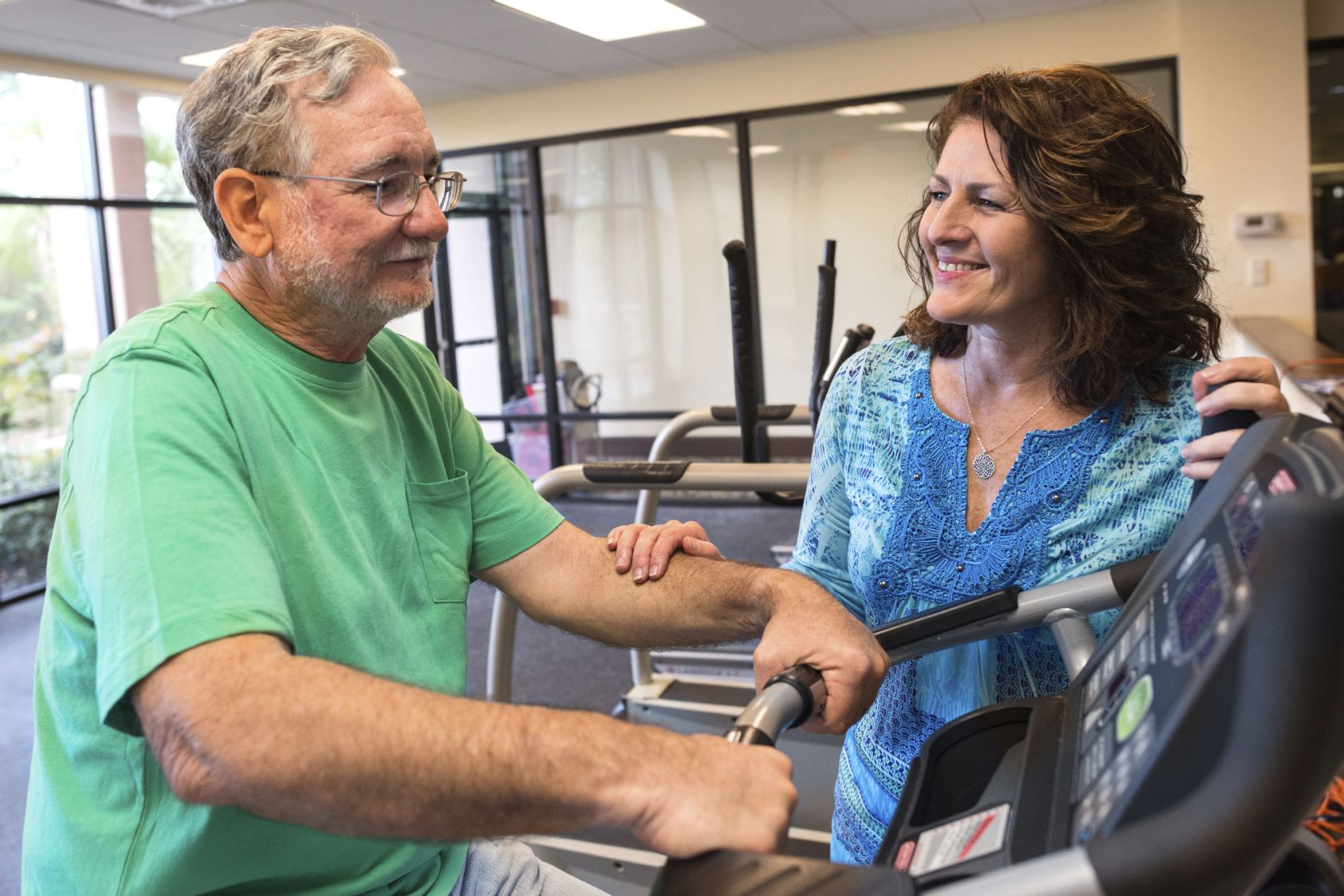 Grey-haired man on a treadmill with a supportive woman nearby